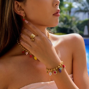 Detail of 18K gold stainless steel fruit charm jewelry set worn by a model poolside