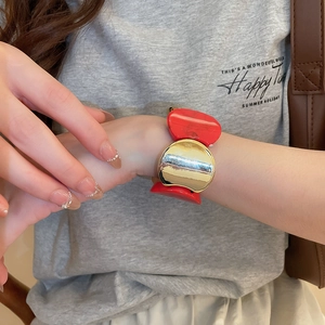 Détail du large bracelet en acrylique rouge et doré porté au poignet avec fini métal
