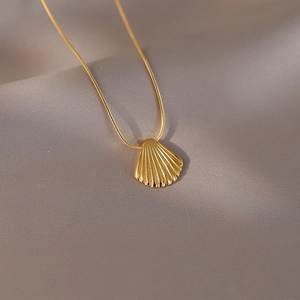 Elegant gold shell pendant on a thin snake chain over luxurious grey silk fabric
