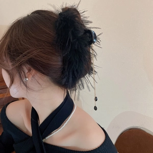 Detail of elegant black feather hair claw with golden chain tassels and drop pendant