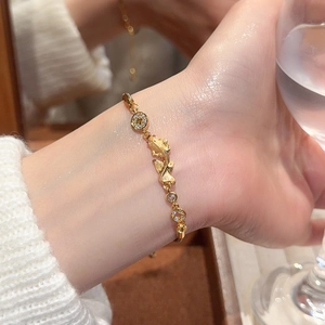 Detailed close-up of a gold fish and coin bracelet with zircons worn on the wrist