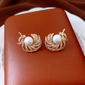 Detailed close-up of 18k gold plated feather earrings with large pearls on silk