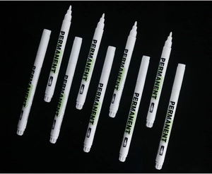 Set of nine white permanent markers with fiber tips scattered on a dark background