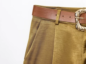 Close-up of olive green satin trousers featuring a brown faux leather belt and gold buckle