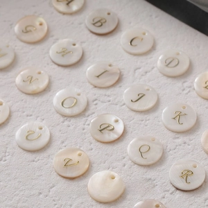 Macro shot of circular freshwater shell letter charms with golden inlay for DIY jewelry