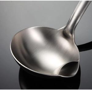 Macro shot of stainless steel soup ladle with a spout on a dark reflective surface