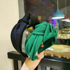 Detail of twisted velvet headband set in black and green colors held by hand