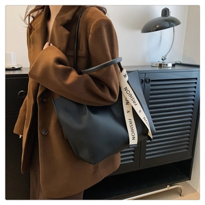 Detail view of a black tote bag with a striped 'FASHION' strap worn on a brown coat