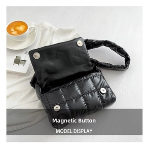 Detail of the magnetic buckle closure on a black quilted puffer shoulder crossbody bag