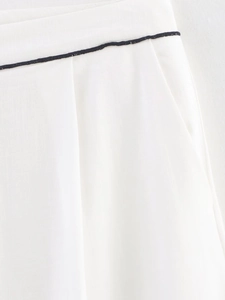 Detail shot of white linen trousers featuring a side pocket and black contrast piping