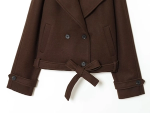 Detail of brown wool-like jacket featuring double-breasted buttons and bow tie hemline