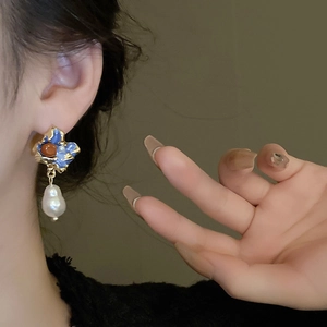 Close-up of vintage baroque pearl earrings with blue enamel and gold-plated details