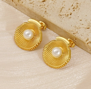 Macro detail of gold shell earrings with white pearl inlay on elegant textured background