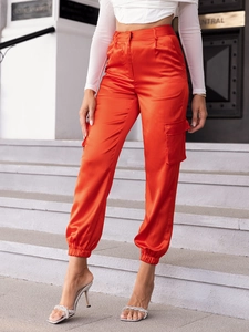 Detail of orange satin cargo pants with elastic waistband and side pocket on steps