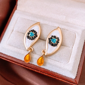 Macro view of gold evil eye stud earrings with an orange teardrop crystal pendant