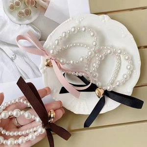 Close-up of pearl ribbon bracelets with gold heart pendants in pink, black, and coffee