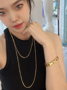 Layered 18K gold square snake bone necklace and screw motif bangle on a female model