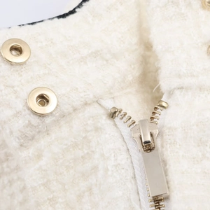 Detailansicht aus nächster Nähe von cremefarbenem Tweed-Stoff mit goldenem Metall-Reißverschluss
