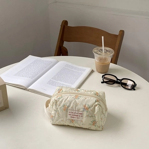 Detail of quilted floral makeup bag with fabric handle on a lifestyle desk setup