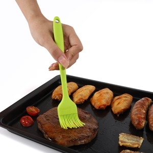 Green silicone basting brush applying sauce to steak and BBQ meat on a dark grill pan