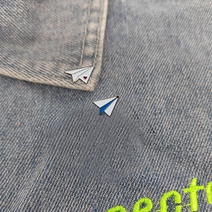 Close-up of cute paper airplane enamel pins with heart and stripe on denim jacket