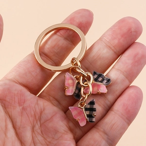 Close-up of pink and black checkered butterfly charms on a gold keychain being held