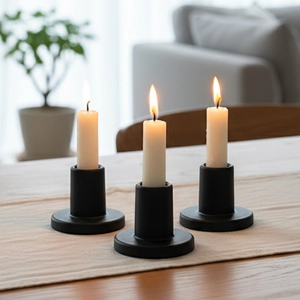 Set di tre candelieri neri minimalisti con candele bianche in un ambiente domestico