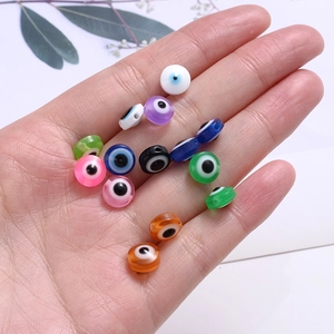 Flat round resin evil eye beads in multiple colors held in hand for DIY jewelry making