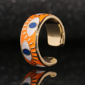 Detail of gold evil eye ring with orange enamel finish and C-shaped adjustable band