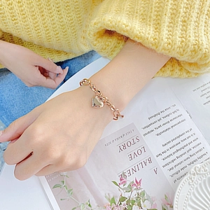 Close-up of a rose gold heart pendant chain bracelet on a wrist over a book background