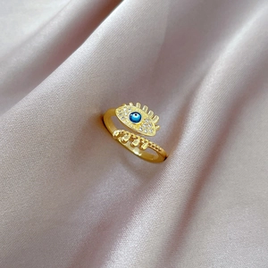 Macro view of gold evil eye ring with blue enamel and pavé crystals on purple silk fabric