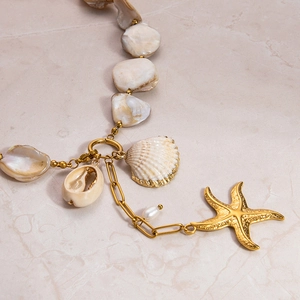 Close-up of gold chain necklace with seashell, starfish charms and white pearls