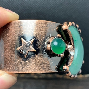 Makroaufnahme einer Retro-Bronzemanchette mit Mond- und Sternmotiven und grünen Edelsteinen