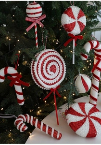 Detail of red and white candy cane foam ornaments hanging on a warm lit Christmas tree