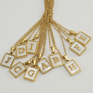 Gros plan de colliers en acier doré avec pendentifs alphabétiques en nacre blanche