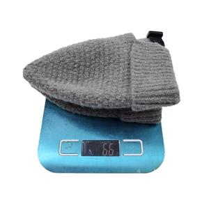 Grey knitted beanie with roll cuff and adjustable buckle weighing 66 grams on a digital scale