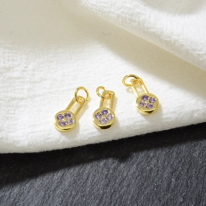 Macro shot of three gold flower pendants with purple zircons on textured fabric background