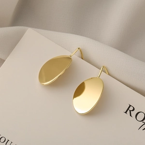 Minimalist gold oval geometric drop earrings with polished metallic finish on beige backdrop