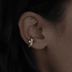 Dettaglio di un ear cuff dorato con perla e texture irregolare sull'orecchio