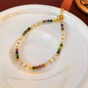 Macro detail of 18K gold plated bead bracelet with multicolored stones on a pearl tray