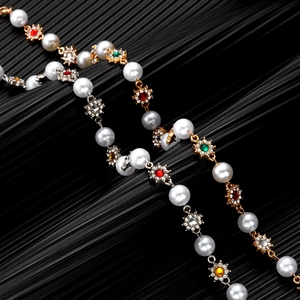 Close-up of pearl and colorful rhinestone flower necklace on a black textured background