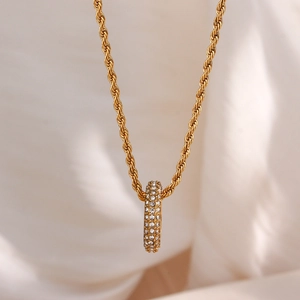 Macro shot of gold twisted rope chain with a pavé zircon cylindrical pendant on fabric