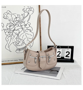 Detail view of beige half-moon crossbody bag with silver zippers and rivet accents
