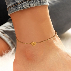 Detailed view of a gold heart anklet with letter B engraving on an ankle.