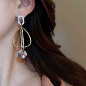 Détail de boucles d'oreilles géométriques en argent et or portées pour un look moderne