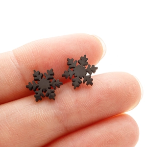 Macro shot of minimalist black snowflake stud earrings held between fingers for scale