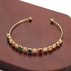Detail of gold-plated bracelet with multi-color zircon stones on a wooden stand
