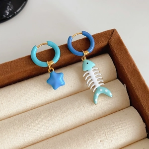 Detail of titanium steel earrings with blue star and fishbone enamel pendants on jewelry box