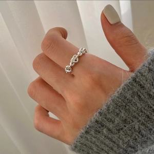 Detail of silver heart knot ring on finger with soft grey sweater and white background