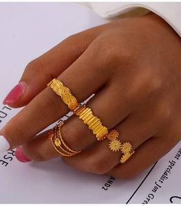 Detailaufnahme von vier goldfarbenen Ringen mit Web- und Blumenmuster an einem Finger